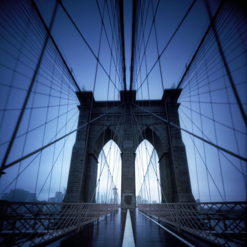 A symmetrical, low-angle view of the Brooklyn Bridge stone towers and suspension cables under a deep blue sky.