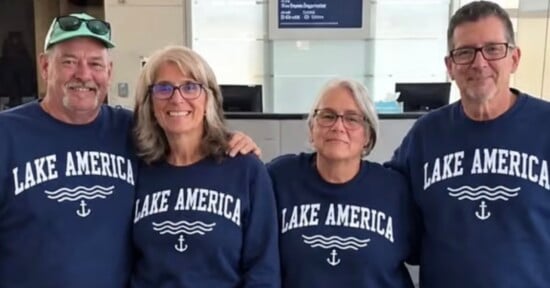 Four people stand side-by-side wearing matching navy blue sweatshirts that say "LAKE AMERICA" with a wave and anchor graphic.