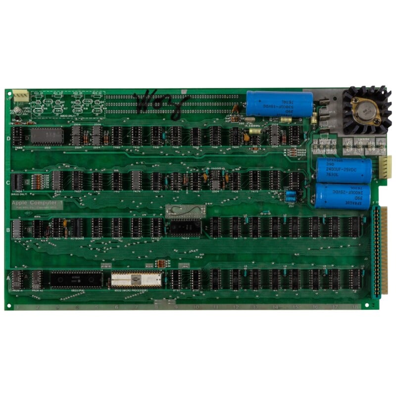 An Apple-1 computer circuit board featuring a 6502 microprocessor, rows of integrated circuits, capacitors, and a heat sink.