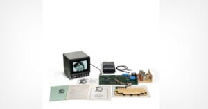 An Apple-1 computer setup including a circuit board, keyboard, monitor displaying a face, cassette recorder, and several manuals on a white background.