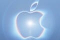 A glowing, iridescent Apple logo centered against a soft, light blue background with circular light flares.