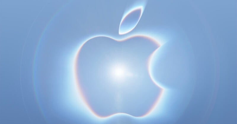 A glowing, iridescent Apple logo centered against a soft, light blue background with circular light flares.
