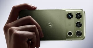A hand holds a green smartphone with a triple-lens camera system and a Motorola logo on the back.