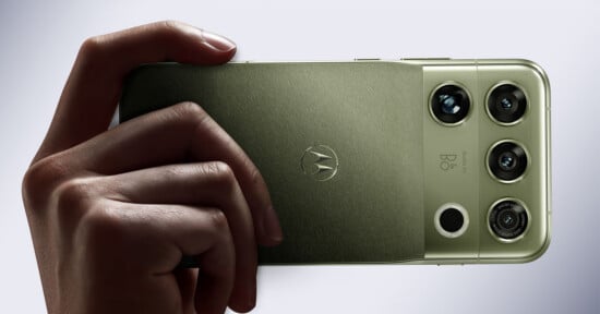 A hand holds a green smartphone with a triple-lens camera system and a Motorola logo on the back.