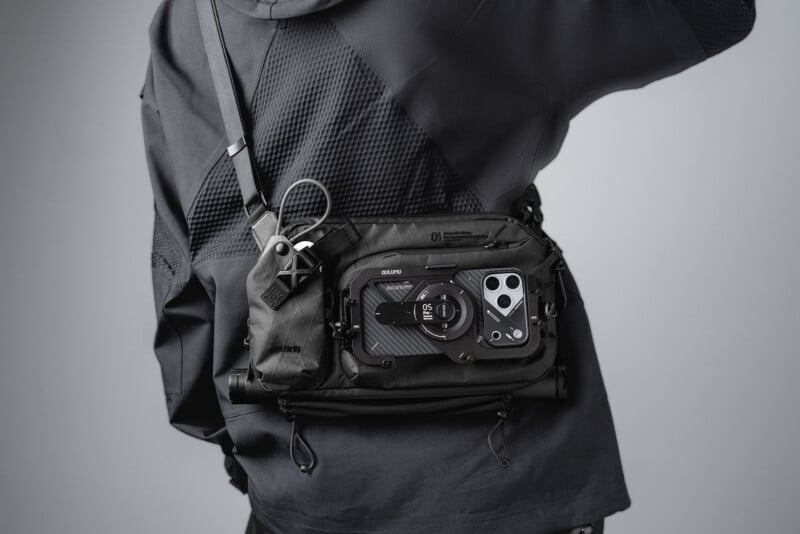A person wearing a black technical sling bag across their chest, featuring an integrated magnetic phone mount holding a smartphone.