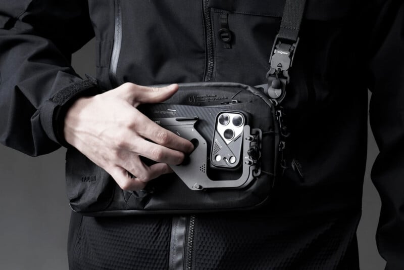 A person wearing a black jacket and a black crossbody bag with a magnetic phone mount attached to the front.