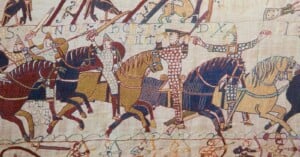 A section of the Bayeux Tapestry showing Norman cavalry on horseback, with archers below and Latin text embroidered above.