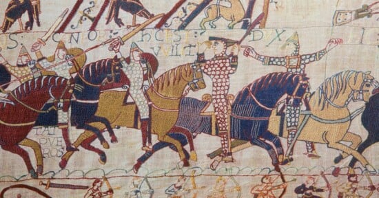 A section of the Bayeux Tapestry showing Norman cavalry on horseback, with archers below and Latin text embroidered above.