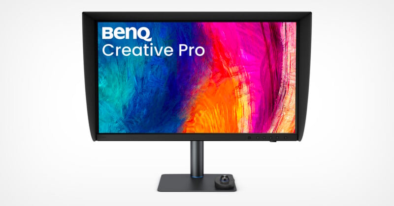 A BenQ Creative Pro monitor with a black shading hood stands on a desk, featuring a colorful abstract display and a circular control dial on its base.