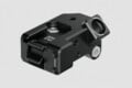 A black, machined metal camera accessory mount featuring a quick-release lever, multiple screw holes, and a circular port on a gray background.