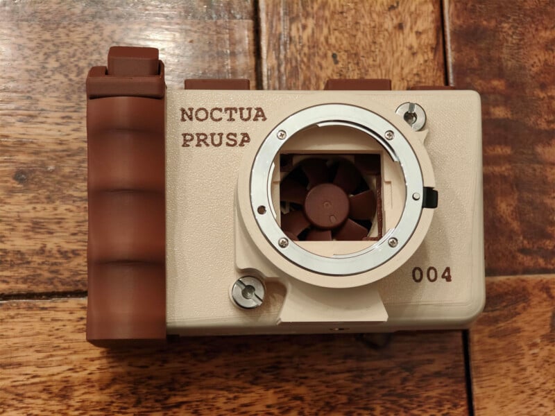 A 3D-printed camera body in Noctua-themed beige and brown, featuring a small cooling fan visible through the lens mount and the text "NOCTUA PRUSA" and "004" printed on the front.