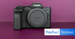 A black Canon EOS mirrorless camera body with a lens cap attached sits against a solid purple background, with a PetaPixel Reviews logo in the bottom right corner.