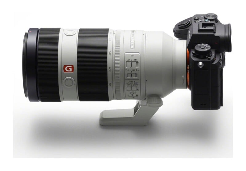 A side view of a white telephoto zoom lens attached to a black mirrorless camera body, set against a plain white background.