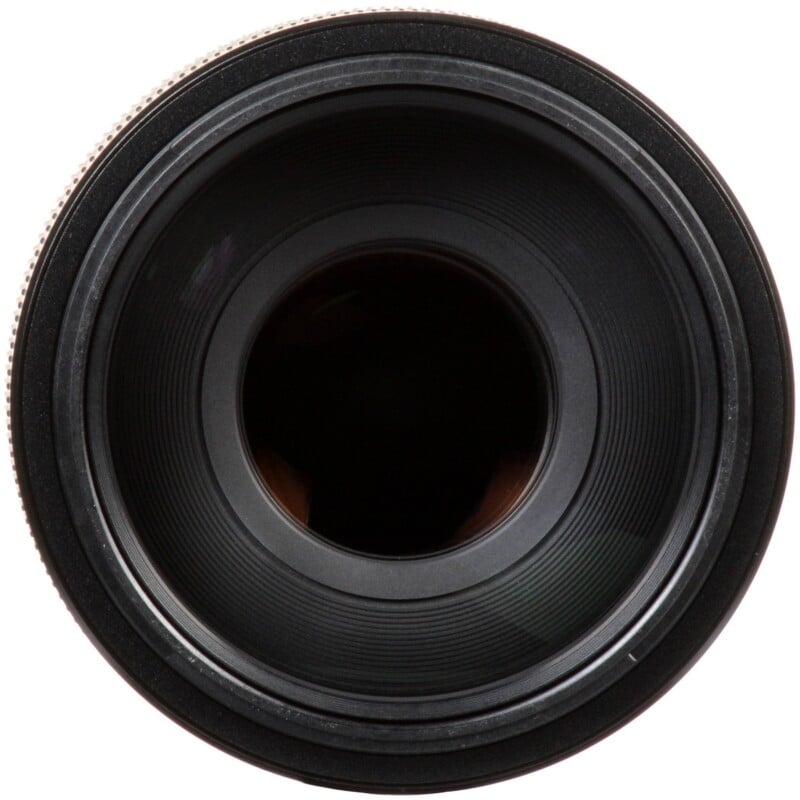 A front-facing view of a black camera lens, showing the circular glass element and the surrounding ridged focus ring.