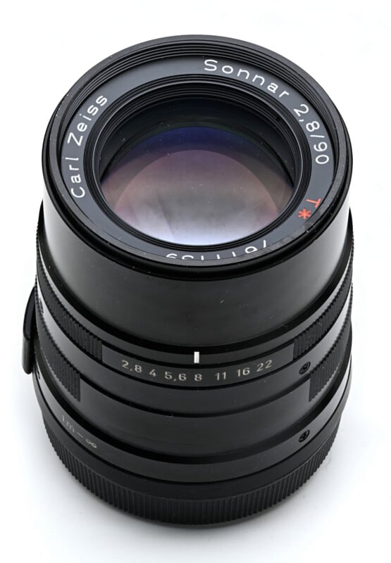 A black Carl Zeiss Sonnar 2.8/90 T* camera lens stands vertically against a white background.