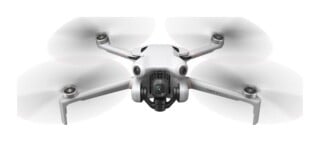 A white DJI Mini 4 Pro drone is shown from the front with its propellers spinning, featuring a central camera gimbal and forward-facing sensors.