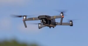 A gray quadcopter drone with spinning propellers flies against a clear blue sky.