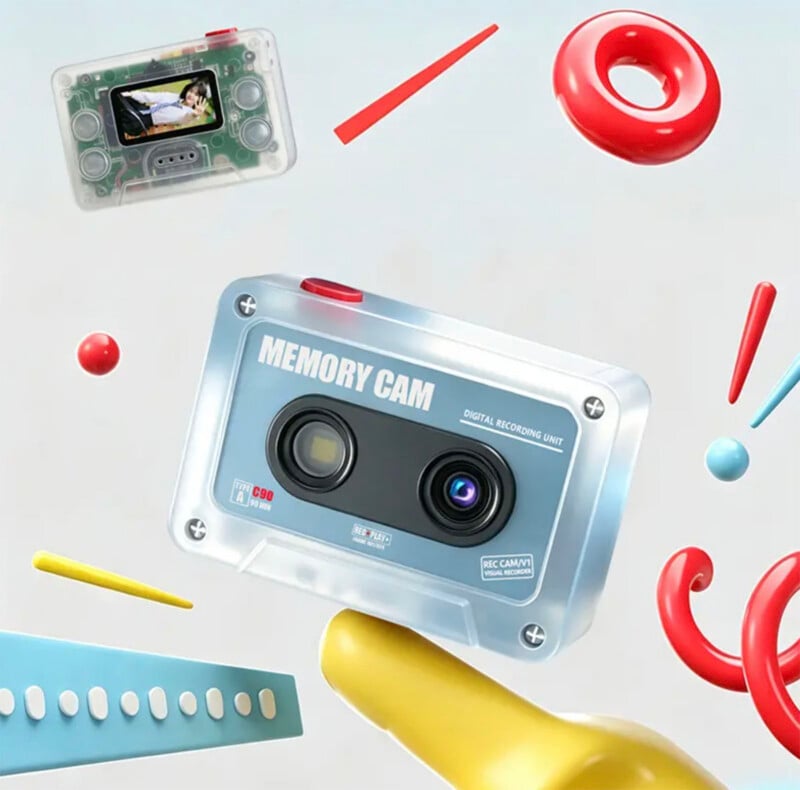 A digital camera shaped like a cassette tape floats in the air alongside a smaller transparent camera, a red ring, and various abstract colorful shapes.