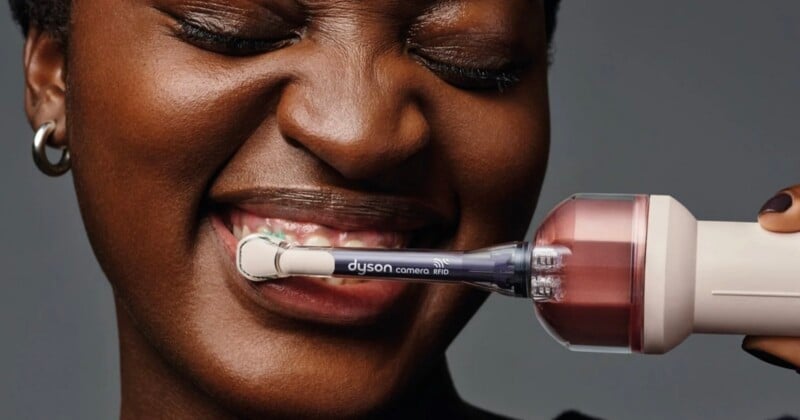 A person smiles while holding a Dyson-branded electric toothbrush with a camera and RFID sensor against their teeth.