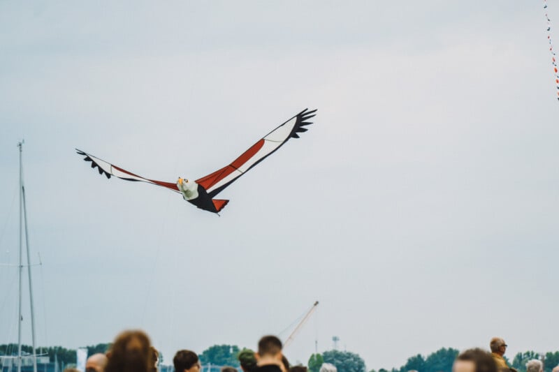 An eagle-shaped kite flies in a cloudy sky above a crowd of people.