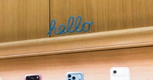 A blue, cursive "hello" sign is mounted on a wooden wall above a shelf displaying several smartphones.