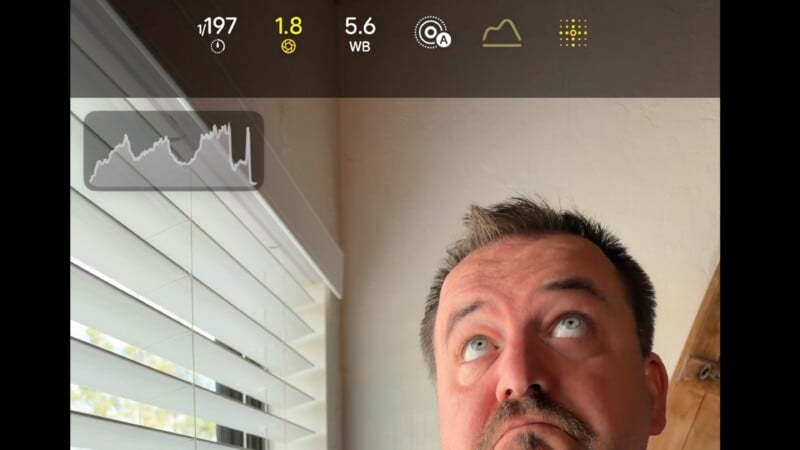 A man looks upward in a room with a window, while a camera interface with a histogram overlay is visible at the top.