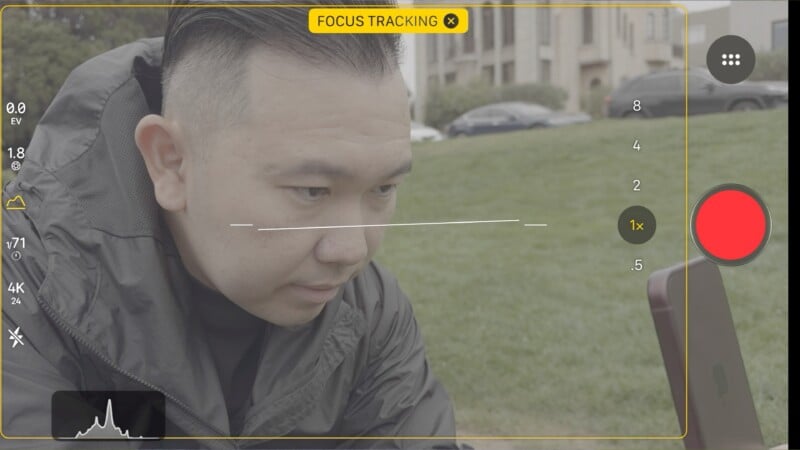 A smartphone camera interface displays a person in a dark jacket looking down, with focus tracking enabled and a histogram visible at the bottom.