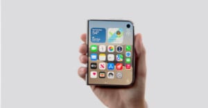 A hand holds a folded smartphone displaying a home screen with app icons, widgets, and a search bar on a light gray background.