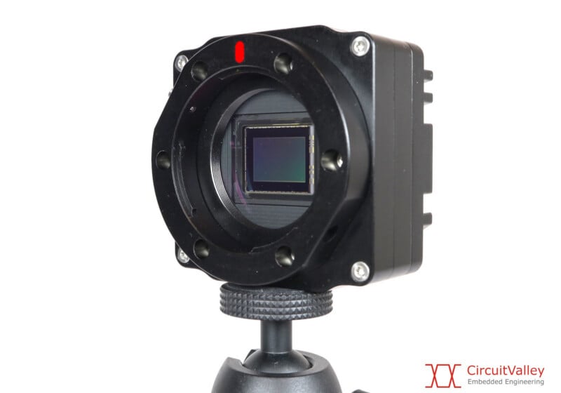 A black industrial camera sensor mounted on a tripod, featuring a circular lens mount and a rectangular image sensor.