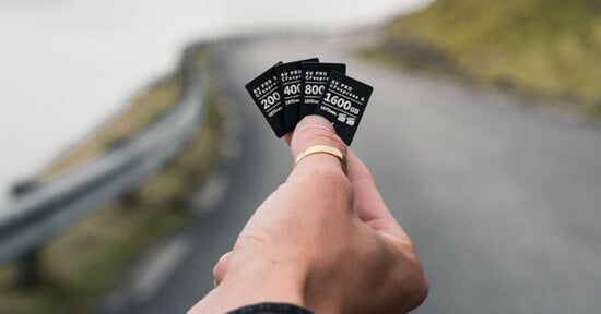 A hand wearing a gold ring holds four CFexpress memory cards of varying capacities—200, 400, 800, and 1600 GB—against a blurred road background.