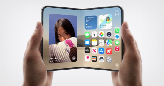 A person holds a foldable smartphone displaying an iOS-style home screen with widgets and app icons against a desert background.