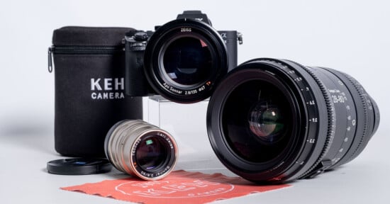 A camera body with a Zeiss lens attached sits behind a smaller silver lens, a large black zoom lens, a KEH Camera branded case, and a red cleaning cloth.