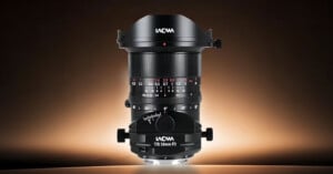 A Laowa T/S 24mm F2 tilt-shift lens stands vertically against a gradient brown background, showing its focus ring, aperture markings, and rotation dials.