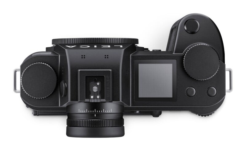 Top-down view of a black digital camera with a lens mount, hot shoe, top status display, and various control dials and buttons.