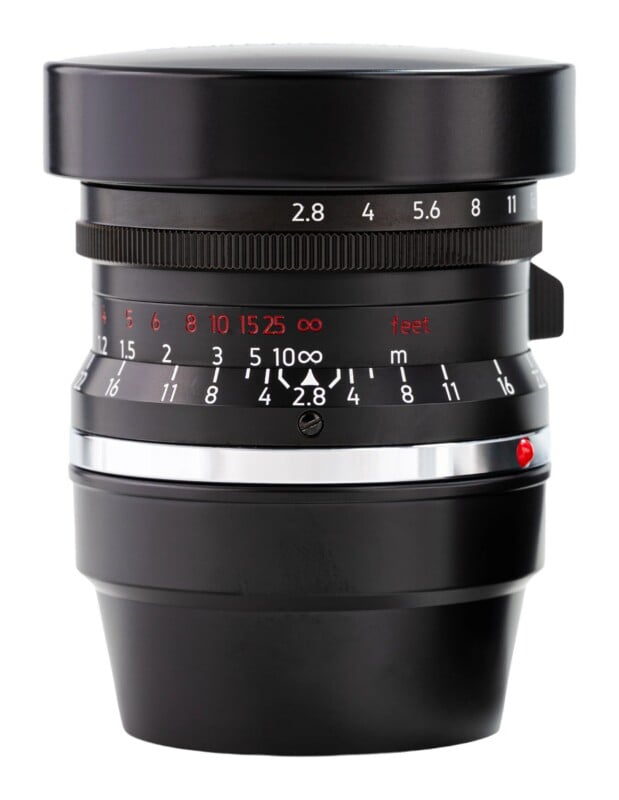 A black camera lens with a silver mounting ring, aperture markings, and distance scales in feet and meters, isolated against a white background.