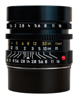 A black camera lens barrel showing aperture settings from 1.4 to 16, distance scales in feet and meters, and depth-of-field lines.