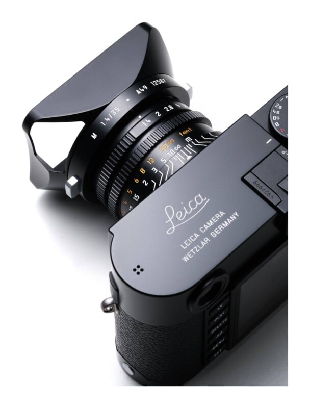 A high-angle, close-up view of a black Leica camera with a 35mm lens and a lens hood, set against a white background.