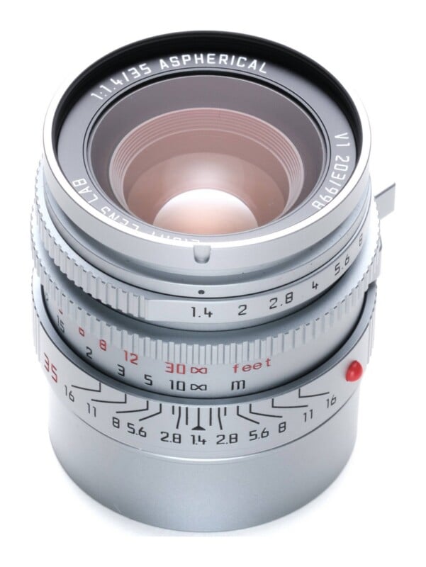 A silver 35mm f/1.4 aspherical camera lens viewed from a high angle against a white background.