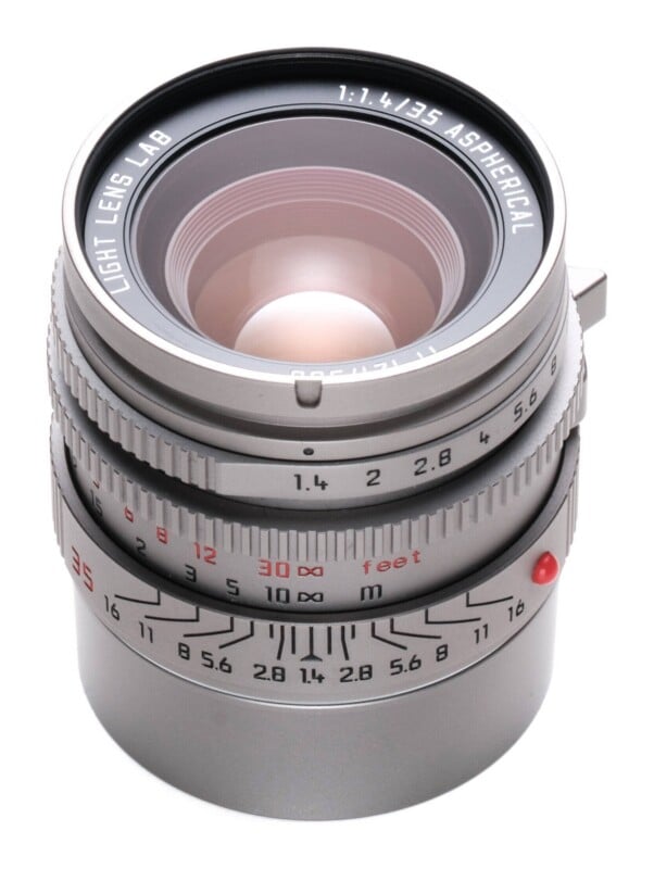 A silver Light Lens Lab 35mm f/1.4 Aspherical manual focus camera lens viewed from a high angle against a white background.
