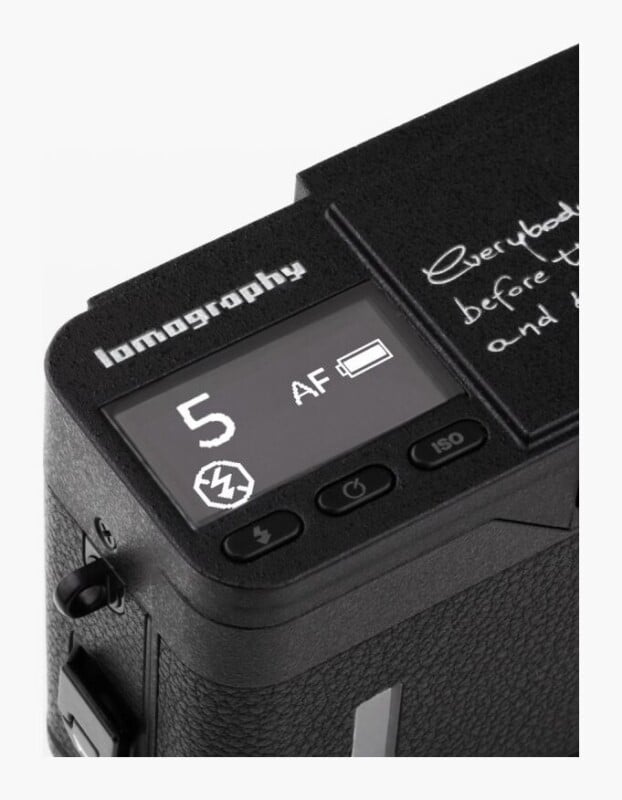 A close-up view of the top control panel of a black Lomography camera, showing an LCD screen with a frame counter at 5, an AF indicator, a battery icon, and a flash-off symbol, alongside three physical buttons labeled with flash, power, and ISO icons.