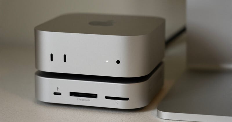 A silver Apple Mac Studio computer sits stacked on top of a matching silver accessory hub with card reader slots.