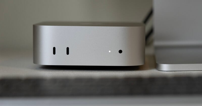 A silver Apple Mac Studio computer sits on a desk, showing two front-facing USB-C ports, a status light, and a headphone jack.