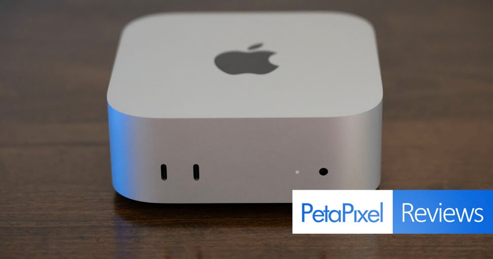 A silver Apple Mac Studio computer sits on a dark wooden surface, showing two front-facing USB-C ports, a status light, and a headphone jack, with a PetaPixel Reviews logo in the bottom right corner.