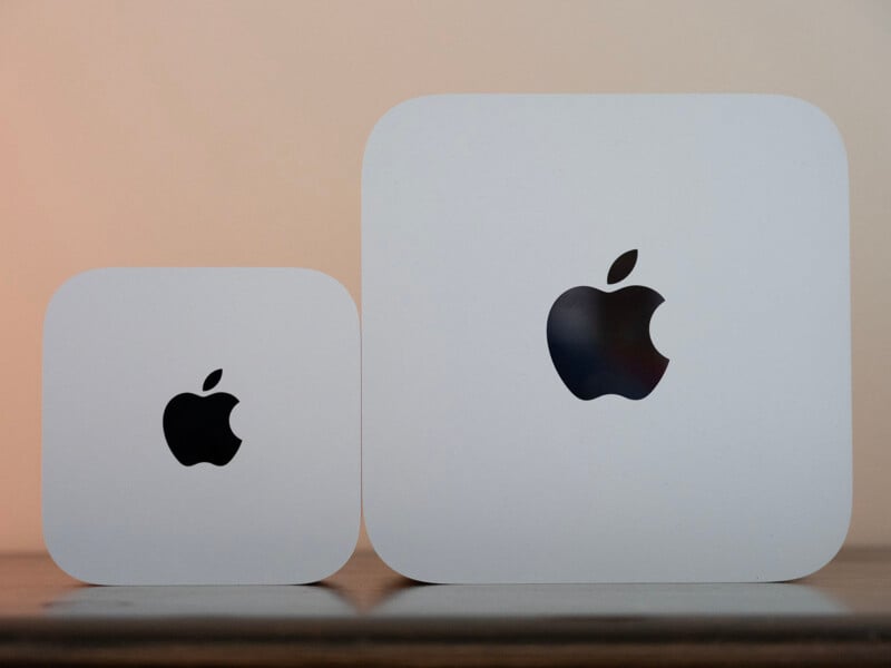 Two white, square-shaped devices with rounded corners and black Apple logos on their tops sit side-by-side on a wooden surface.