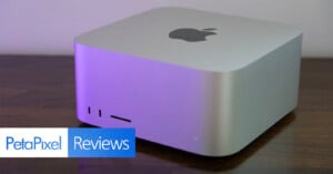 A silver Apple Mac Studio computer sits on a dark wooden surface, with a PetaPixel Reviews logo in the bottom left corner.