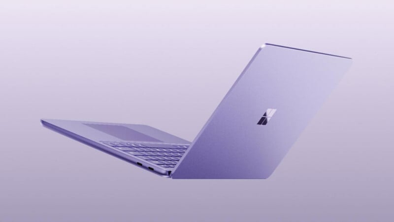 A light purple laptop is angled open against a matching light purple background, showing the back of the lid with a Microsoft logo and a partial view of the keyboard and trackpad.