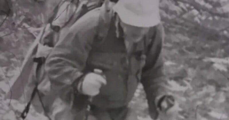 A person wearing a bucket hat and a heavy backpack hikes uphill while using trekking poles.