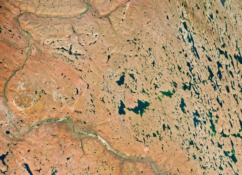 An aerial view of a rugged, arid landscape featuring a winding river, numerous scattered lakes, and rocky terrain.