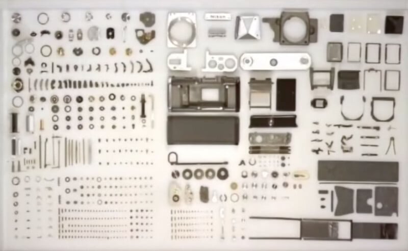 A disassembled camera is laid out in organized rows and columns of individual parts on a white surface.