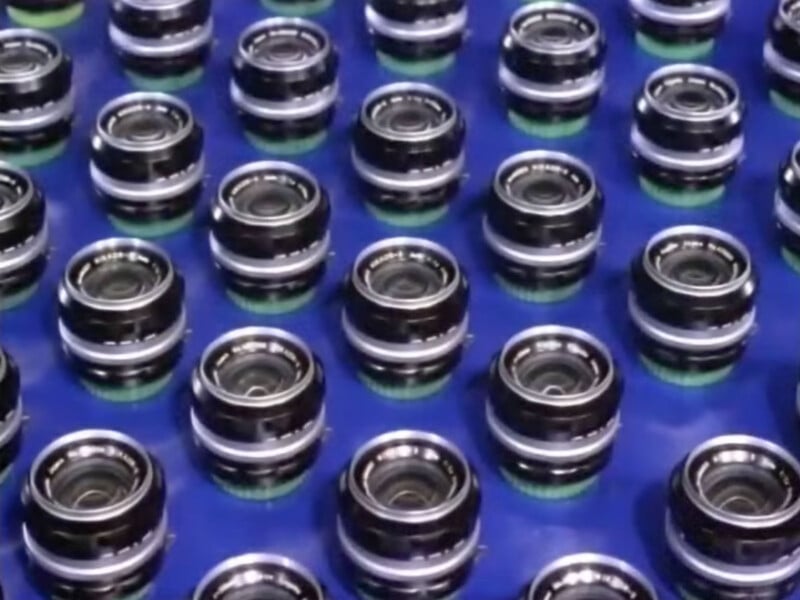 A grid of identical black camera lenses arranged on a blue surface.
